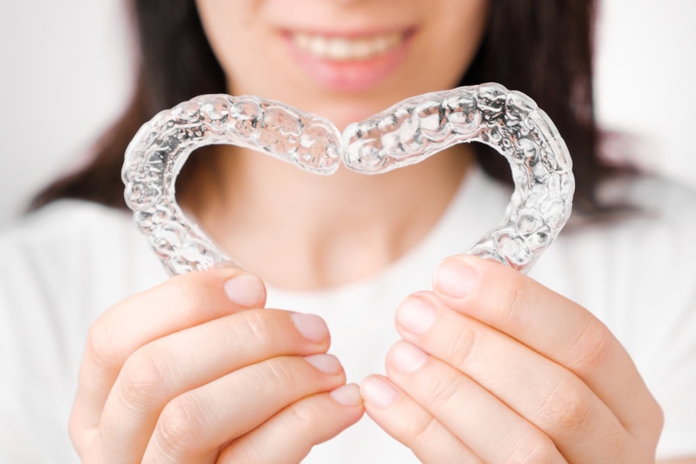 Woman holding two Invisalign aligners shaped like a heart, symbolizing effective treatment for closing smile gaps in adults.