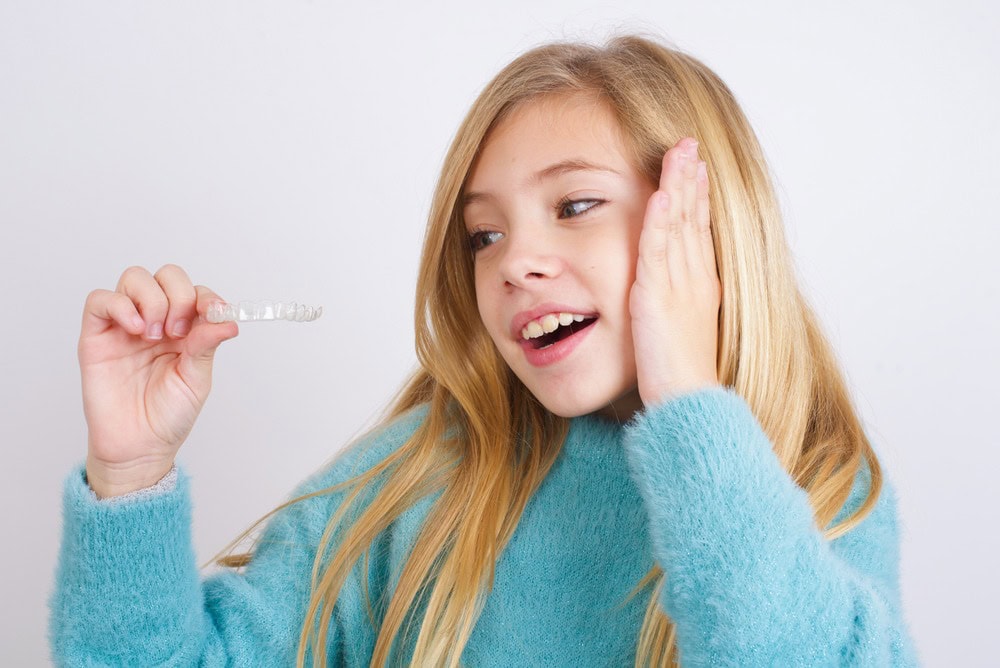 Child holding Invisalign clear aligners fix jaw alignment treatment